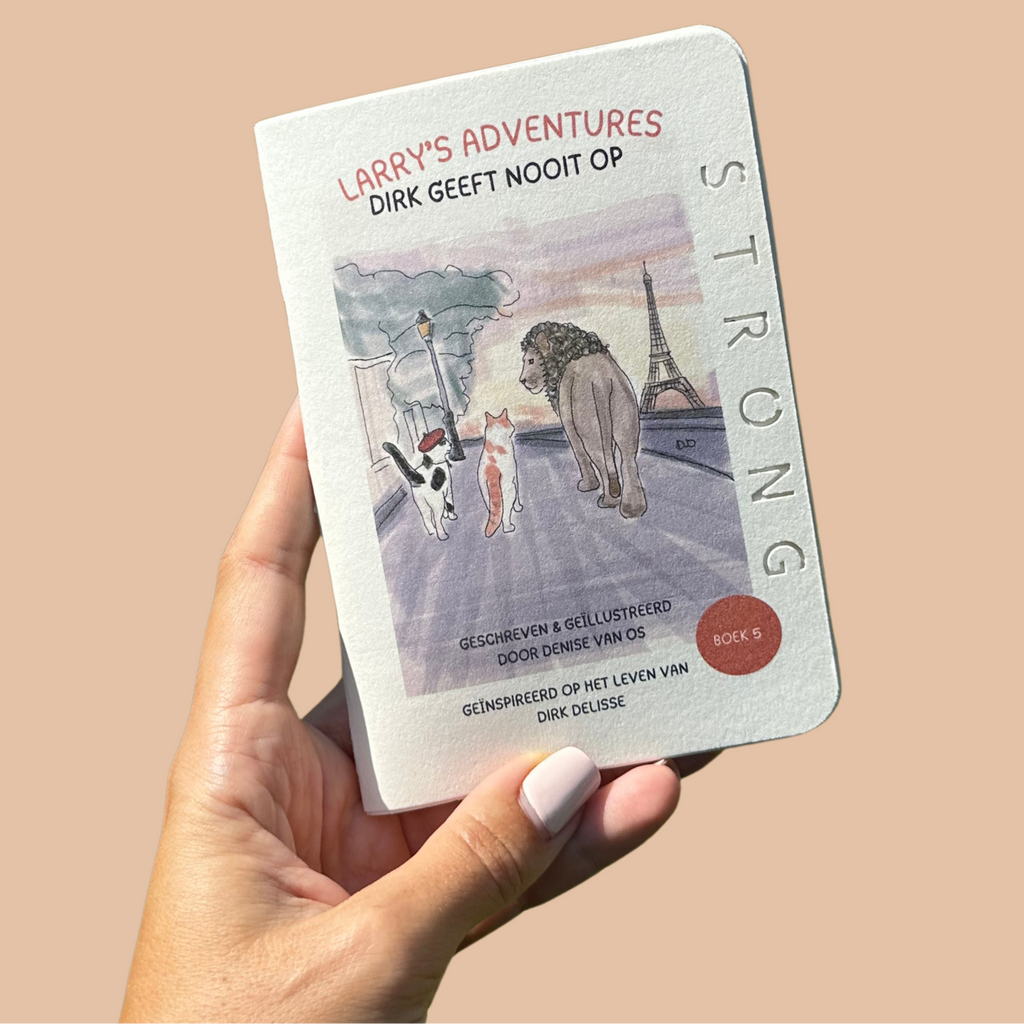 A hand holds a small white notebook or book cover against a solid warm beige background. The cover reads "LARRY'S ADVENTURES" and "DIRK GEEFT NOOT OP" with an illustrated scene showing a CAT, a cat, and a LION, plus the word "STRONG" running vertically.