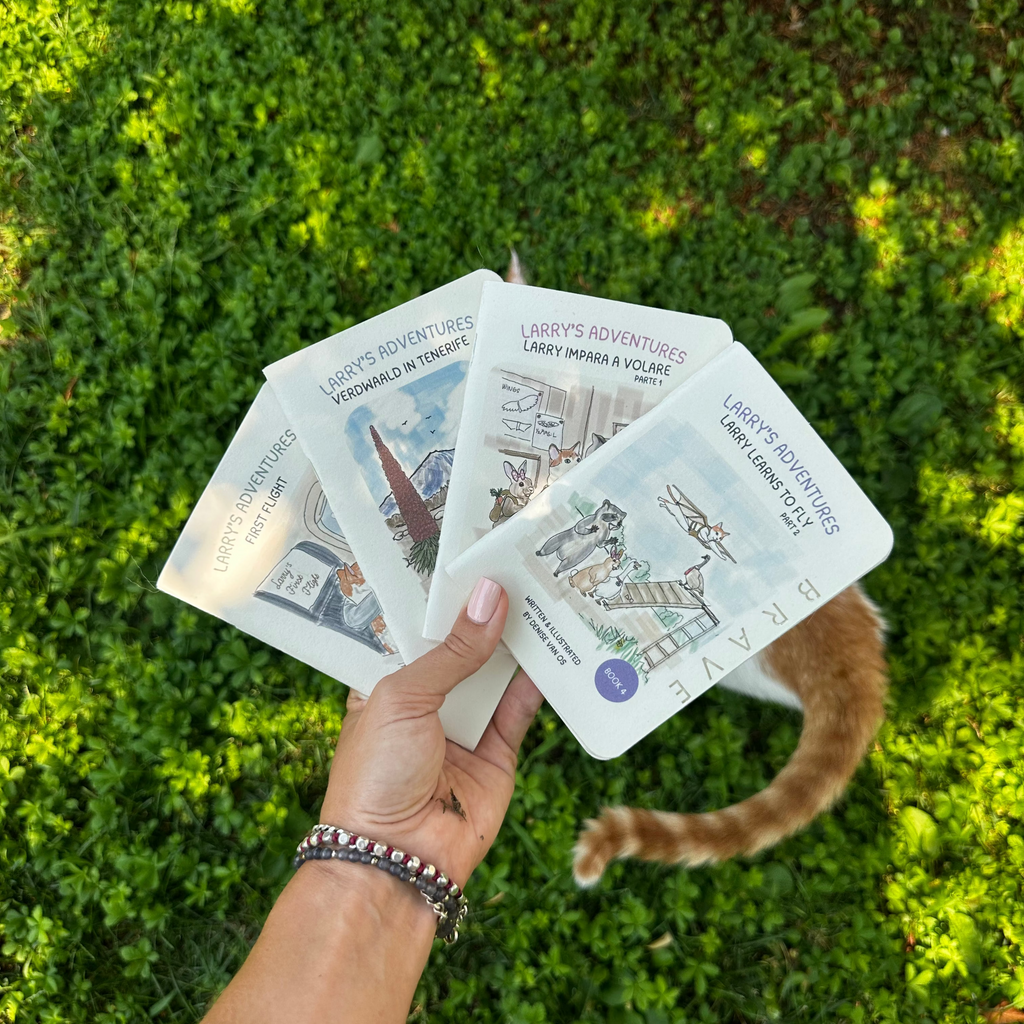 A hand holds three copies of 'Larry's Adventures books against a background of green grass with a cat's tail visible on the right.
